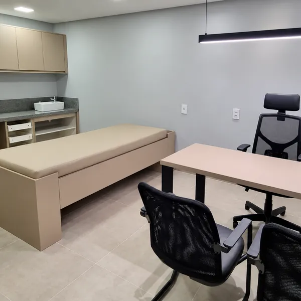 Consultório da Máxima Centro Médico com mesa de atendimento e maca