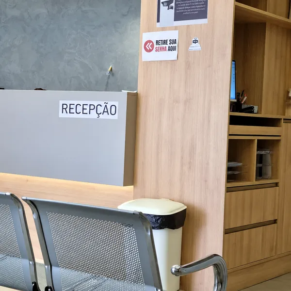 Balcão da recepção em madeira clara com ponto de retirada de senha